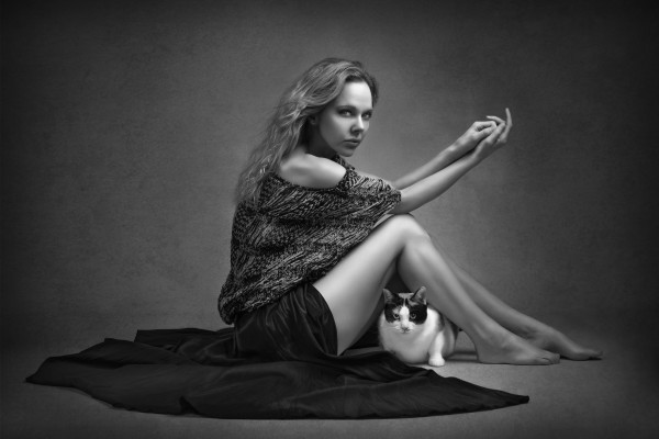 Black and white portrait of a beautiful young woman with a long black skirt sitting on the floor with her domestic cat both looking at the camera by Artmood Visualz